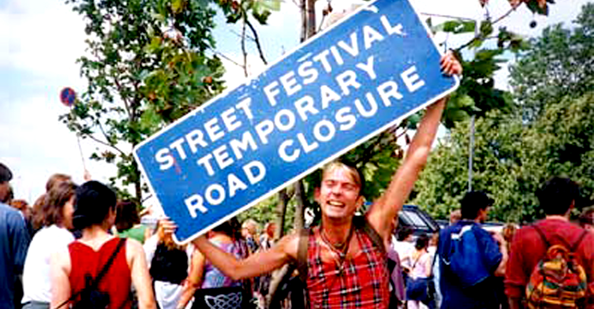 Reclaim the Streets party protest at the M41, London 13 July 1996. An attendee holds a sign reading 'street festival temporary road closure'.